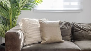 A grey leather sofa with a beige throw blanket and a pillow, positioned next to a potted plant.