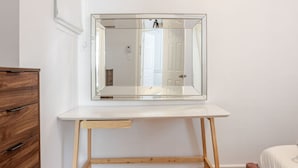 A bedroom with a wooden dresser, a bed, and a desk with a mirror.