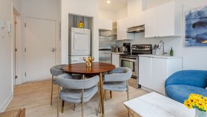 A modern kitchen with white cabinets, a built-in oven, and a stove. There is a dining table with chairs and a vase of flowers.