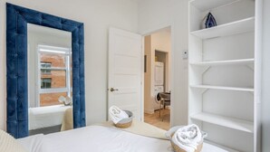 A bedroom with a large bed, a wardrobe, a mirror, and a view of a laundry room.