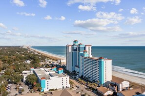 Un hôtel situé sur la côte, composé de plusieurs bâtiments, offrant une vue sur la plage et bénéficiant d’un ciel dégagé.