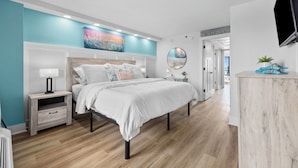 Une chambre à coucher moderne avec un lit, des tables de chevet, un téléviseur et des œuvres d’art accrochées au mur.