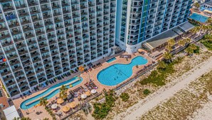 Un hôtel de grande hauteur doté de nombreux balcons, d’un espace piscine avec des chaises longues et offrant une vue sur la plage.