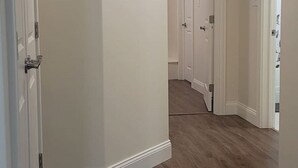Um corredor com piso de madeira, paredes brancas e um quadro pendurado na parede.