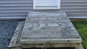 Uma porta branca com uma fechadura e um cadeado, um pequeno banco de jardim e um candeeiro fixado na parede.