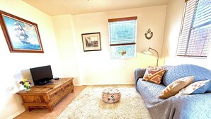 Un salon comprenant un canapé, un pouf, une table basse en bois et un téléviseur posé sur un meuble.