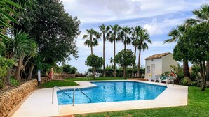Une piscine dotée d’une terrasse carrelée, entourée de pelouse et de palmiers.