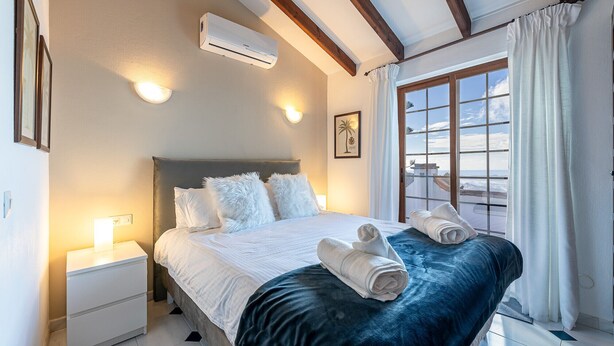 Une chambre d’hôtel avec un lit, une table de chevet, un appareil de climatisation, une fenêtre avec des rideaux et un tableau encadré au mur.