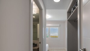 A narrow hallway leading to a bathroom with a window, a door with a handle, and a ceiling light.