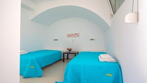 A room with two beds, a small table, and a wall-mounted light fixture.