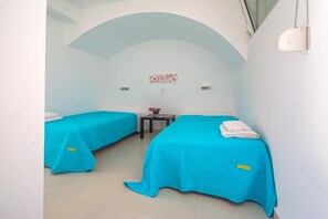 A room with two beds, a small table, and a wall-mounted light fixture. - Country House 'Kaladi Rock Avlemonas' with Sea View. (Avlemonas)