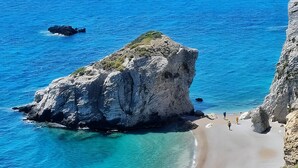A coastal beach with clear blue waters, rocky cliffs, and a sandy shore.