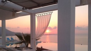 A beachside lounge with sun loungers, a palm tree, and a view of the sunset over the sea.