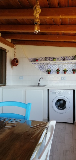 Une cuisine équipée d’un lave-linge, avec une chaise bleue et un plafond en bois.