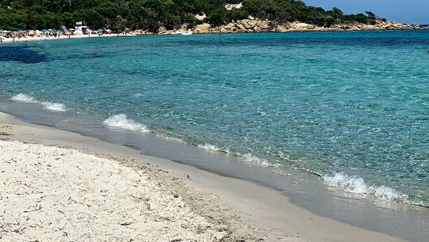 Une plage à l’eau turquoise et limpide, un rivage sablonneux et une structure en forme de château, perchée sur une colline.