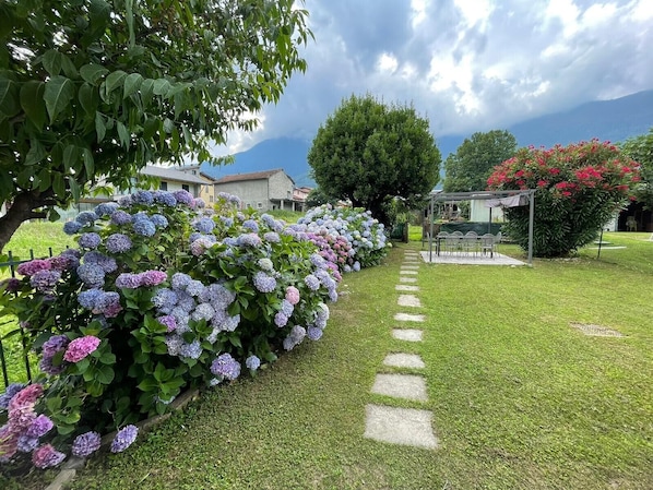 Un jardín con arbustos de hortensia, un sendero de piedra y un pabellón.