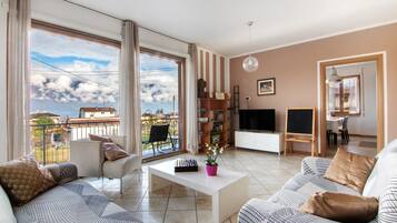 Un salon comprenant un canapé, une table basse, un téléviseur, une bibliothèque et un balcon avec vue.