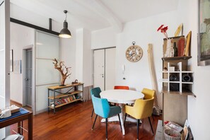 Een eetruimte met een ronde tafel, stoelen, een houten vloer, een boekenkast en een wandklok.