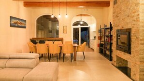 Un espace repas avec un plafond en bois, une cheminée en briques et, au fond, une cuisine moderne.