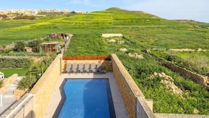 Une piscine bordée d’un mur en pierre, offrant une vue sur un paysage verdoyant avec des bâtiments en arrière-plan.