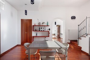 Un comedor moderno con una mesa de vidrio, sillas, una puerta de madera, un estante con adornos y una escalera.