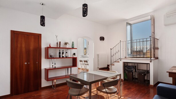 Un espacio habitable moderno con zona de comedor, suelo de madera, una escalera a un nivel superior y vistas a través de un ventanal grande.