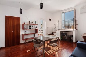 Un espacio habitable moderno con zona de comedor, suelo de madera, una escalera a un nivel superior y vistas a través de un ventanal grande.