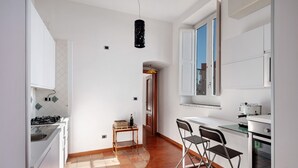 Una cocina con gabinetes blancos, estufa, pileta y un comedor con sillas.