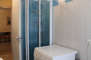 Un baño con ducha compartimentada por vidrio, un lavamanos blanco y pared de azulejos.
