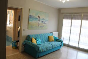 A living room with a sofa, a painting, and a view through a window.