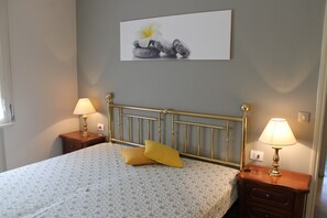 Un dormitorio con una cama, dos mesitas de noche con lámparas, un cuadro en la pared y una mesita de noche con cajón.
