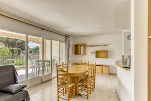 Un coin repas avec une table et des chaises en bois, un canapé et une vue sur une terrasse extérieure, accessible par une porte vitrée.