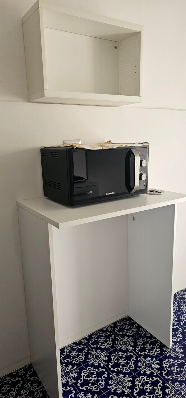 A black microwave on a white table in a room with patterned blue and white floor tiles.
