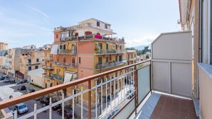 Un balcon offrant une vue sur un immeuble à plusieurs étages, lui-même doté de balcons, une rue en contrebas et un ciel dégagé.