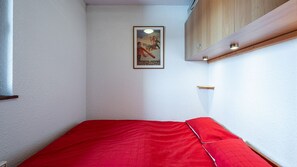 Una stanza piccola con un letto singolo, un poster al muro e un armadietto di legno.