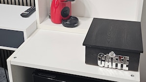 Pieni keittiönurkkaus, jossa on kahvinkeitin, vedenkeitin ja kahvilaatikko valkoisessa kaapissa.