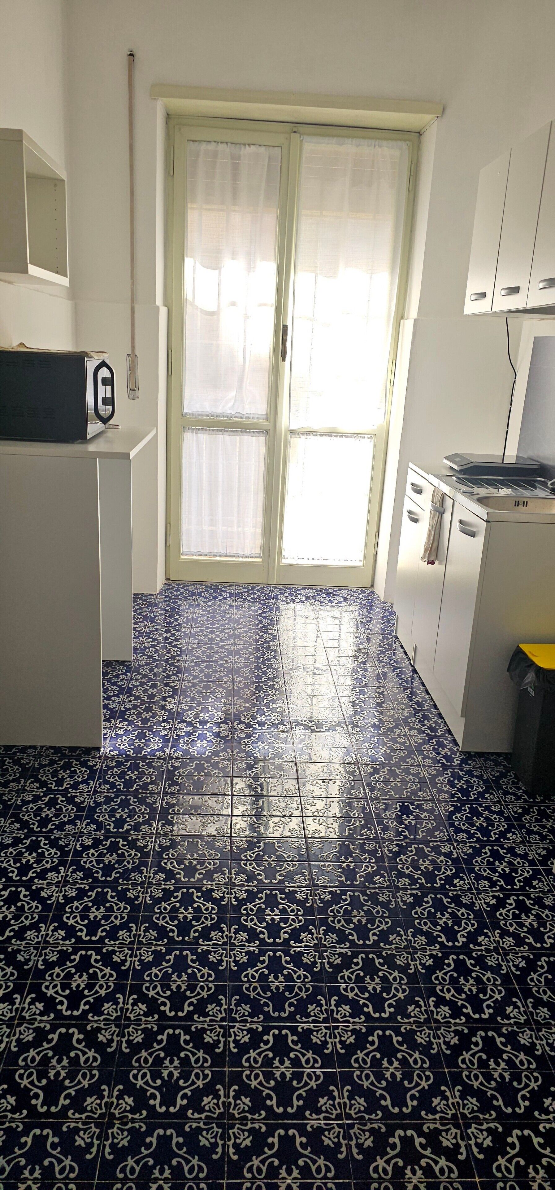 A kitchen with patterned blue and white tiles, a microwave, a stove, and a window with sheer curtains.
