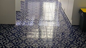 Keittiössä on kuviollisia sinivalkoisia laattoja, mikroaaltouuni, liesi ja ikkuna, jossa on ohuet verhot.