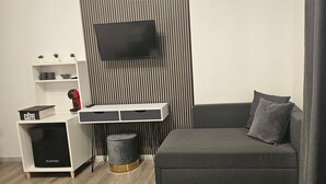 A modern living room with a grey sofa, a small round stool, a white storage unit, and a mounted TV. - Room 'Tripla' with Shared Terrace, Wi-Fi and Air Conditioning (Roma)