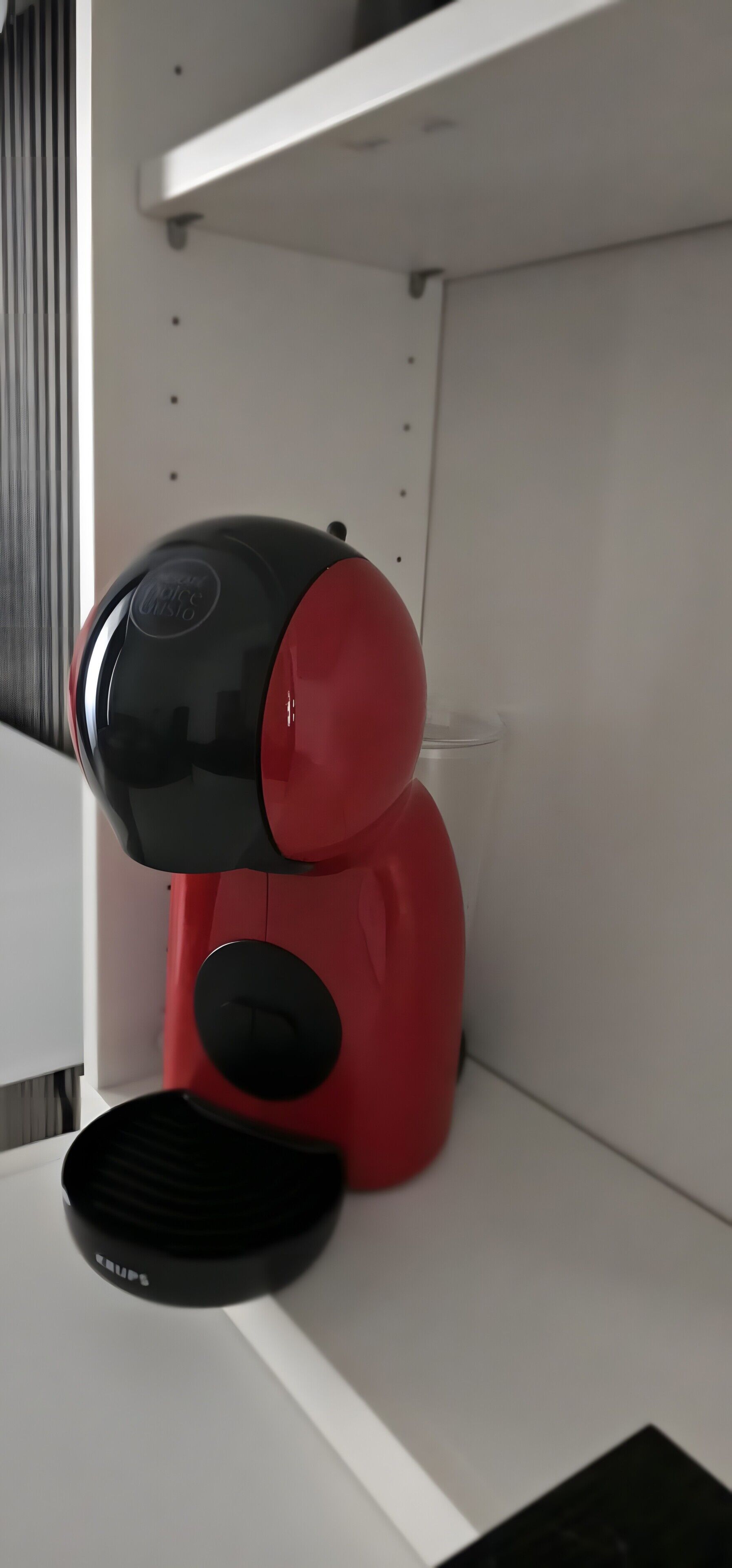 Una máquina de café roja y negra sobre una estantería blanca.