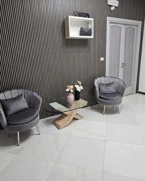 A modern room with two grey armchairs, a wooden coffee table with a vase of flowers, and a white shelf with a sign above. - Room 'Tripla' with Shared Terrace, Wi-Fi and Air Conditioning (Roma)