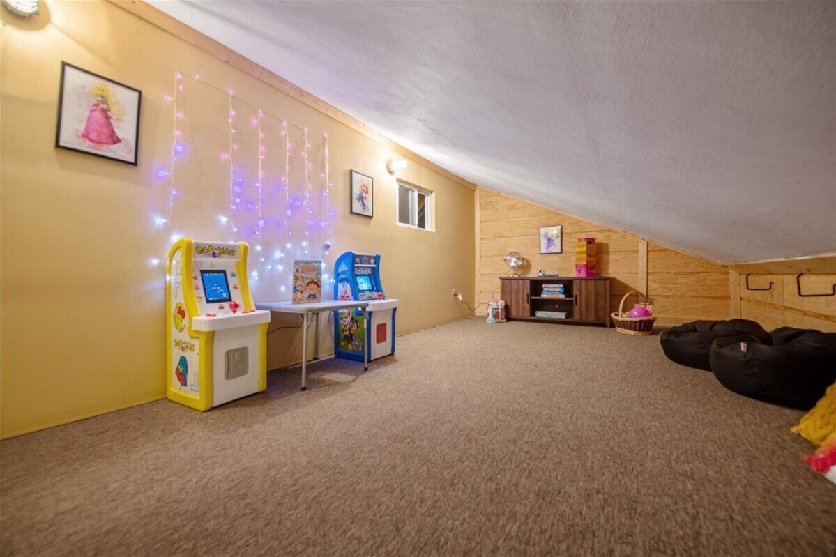 Um quarto de sótão aconchegante, com chão coberto de carpete, parede de madeira e teto. Há duas estações de brincadeiras infantis, uma mesa pequena e sacos de feijão.