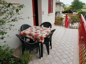 Un balcon avec une table et des chaises, une balustrade rouge et une vue sur les environs.