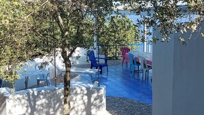 Eine Terrasse im Freien mit Tisch und Stühlen, umgeben von Bäumen und Blick aufs Meer.