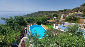 Ein Pool, umgeben von Grünpflanzen, einer Steinsäule und Blick aufs Meer.