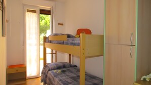A bunk bed room with a door leading to a balcony, a small table, and a cabinet. - Apartment 'Simma' with Balcony and Air Conditioning (SAN MICHELE AL TAGLIAMENTO)