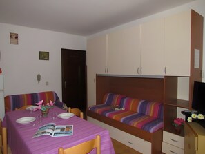 A room with a dining table, chairs, a sofa, a TV, and a cabinet.
