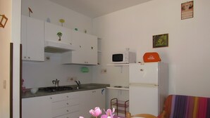 A small kitchen with white cabinets, a microwave, and a refrigerator. There is a dining table with chairs and a vase of flowers. - Apartment 'Simma' with Balcony and Air Conditioning (SAN MICHELE AL TAGLIAMENTO)