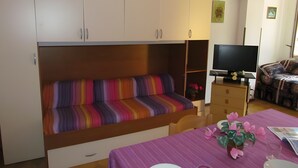 A room with a sofa bed, a television, a dining table with chairs, and a patterned sofa. - Apartment 'Simma' with Balcony and Air Conditioning (SAN MICHELE AL TAGLIAMENTO)