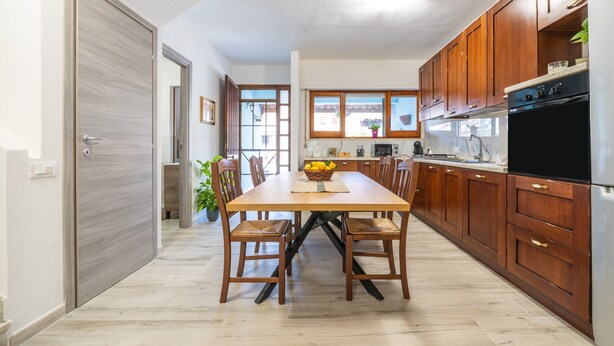 A modern kitchen with wooden cabinets, a dining table with chairs, and a large window. - Casa Vacanze 'EliFra' with Private Terrace, Garden, and Balcony (San Giovanni Suergiu)